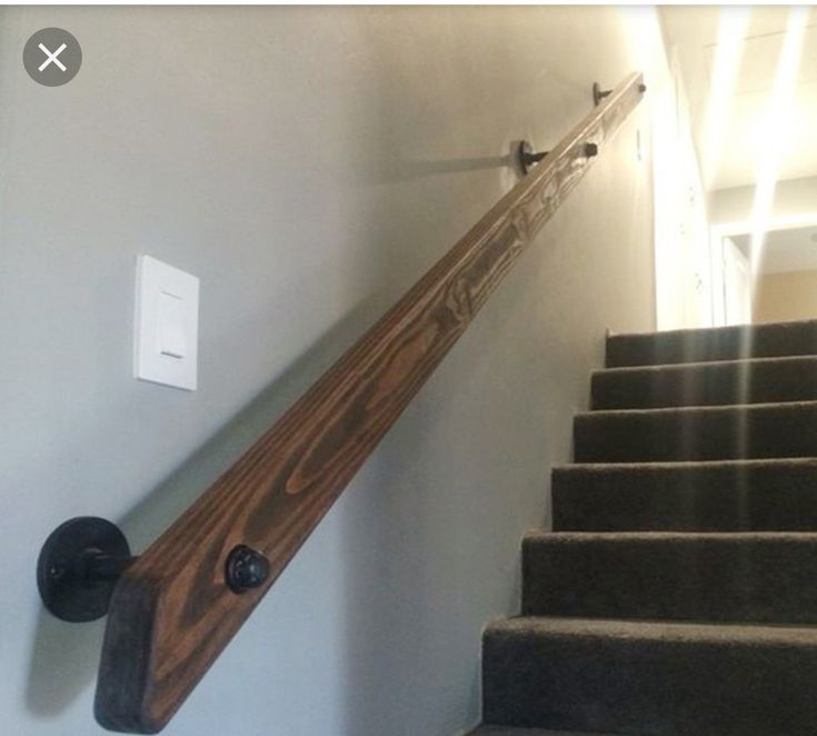 a wooden stair rail on the side of a wall next to a light switch and stairs