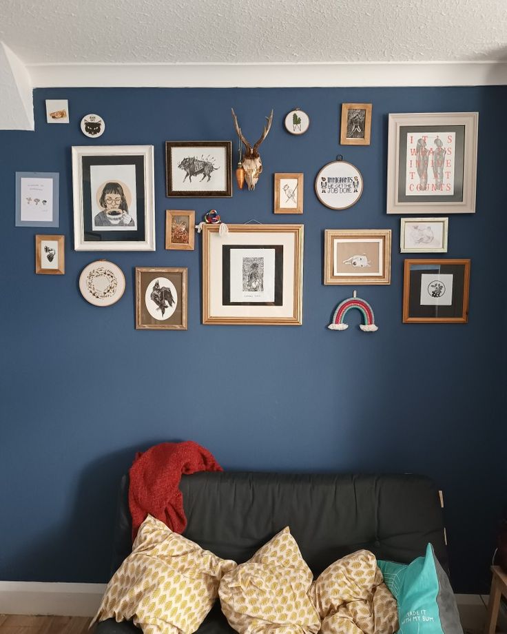 a living room filled with lots of framed pictures on the wall above a black couch