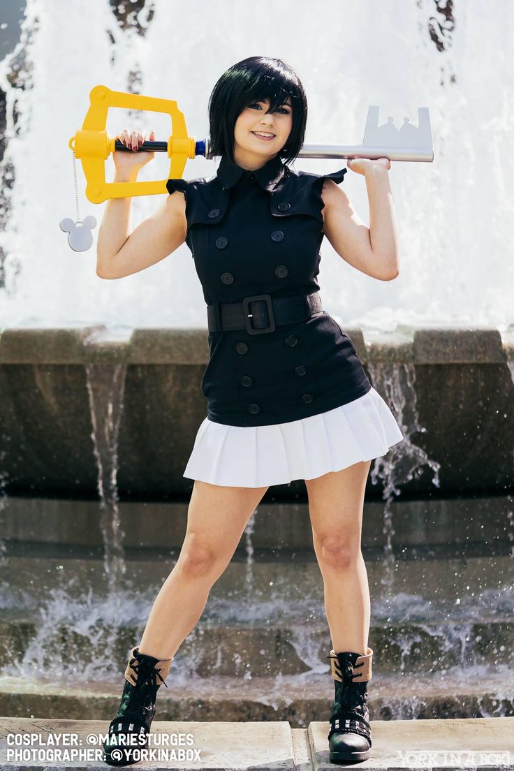 a woman in black and white outfit holding a yellow key over her head while standing next to a fountain