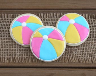 two decorated cookies with beach balls on them sitting on a wooden table next to a piece of cloth