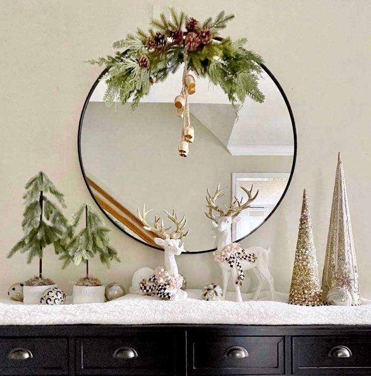 a christmas mantle with deer, pine cones and evergreens in front of a round mirror