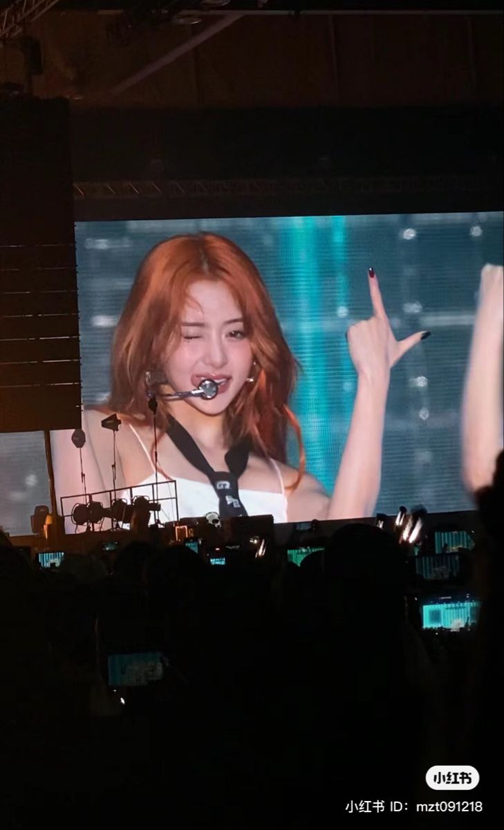 a woman with her hand up in front of a large screen on the stage at a concert