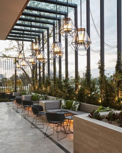 an outdoor seating area with tables and chairs, surrounded by tall glass windows that overlook the city