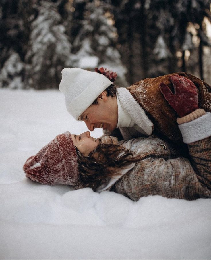 a man and woman laying in the snow kissing