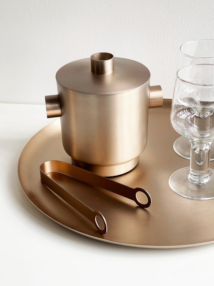 a gold tray with two wine glasses and a teapot on it next to a pair of scissors