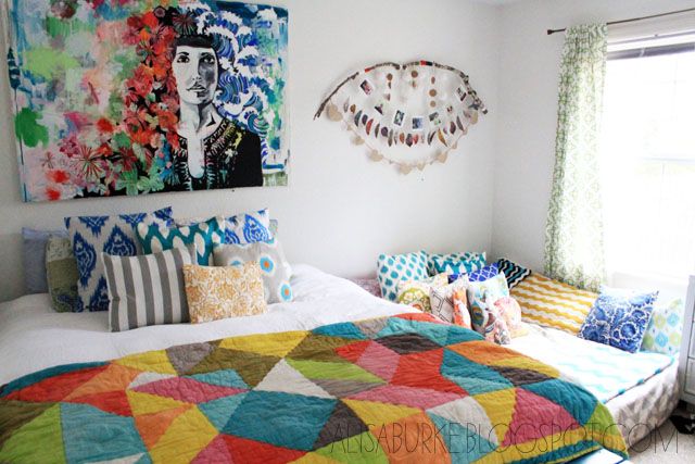 a bed sitting in a bedroom next to a window with paintings on the wall above it