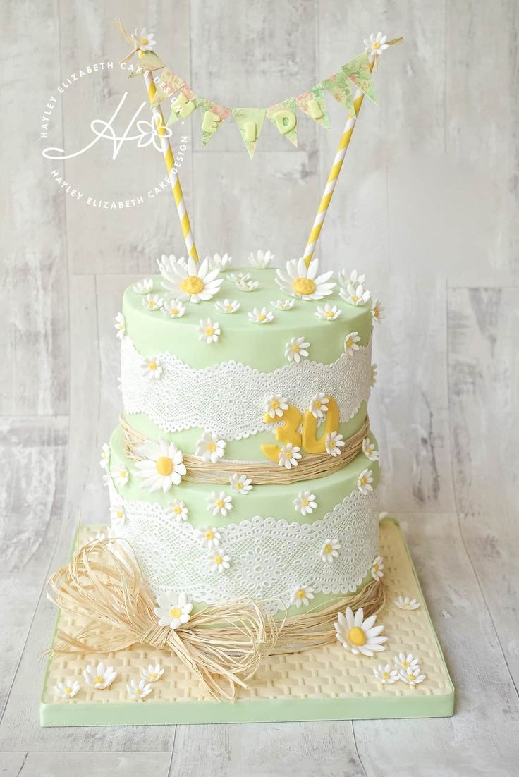 a three layer cake with daisies and bunting on the top is decorated in pastel green