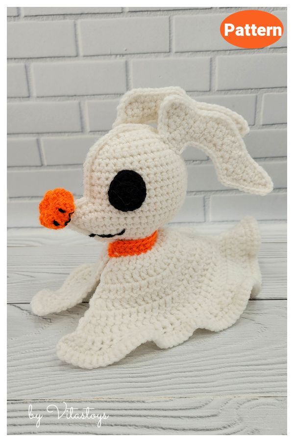 a crocheted white dog with an orange collar sitting on top of a wooden floor