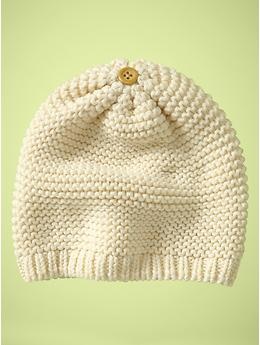 a white knitted beanie with a button on the front and side, against a green background