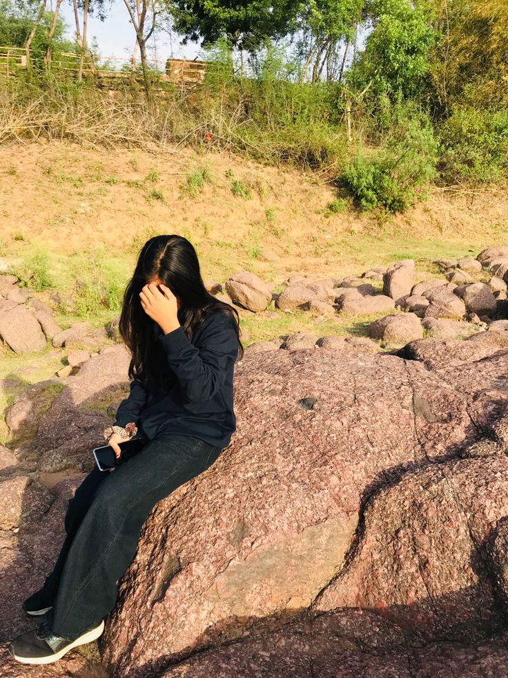 a woman sitting on top of a large rock