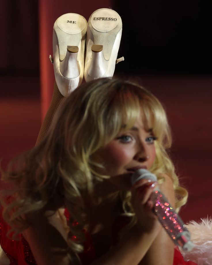 a woman in red dress with white shoes on top of her head and holding a microphone