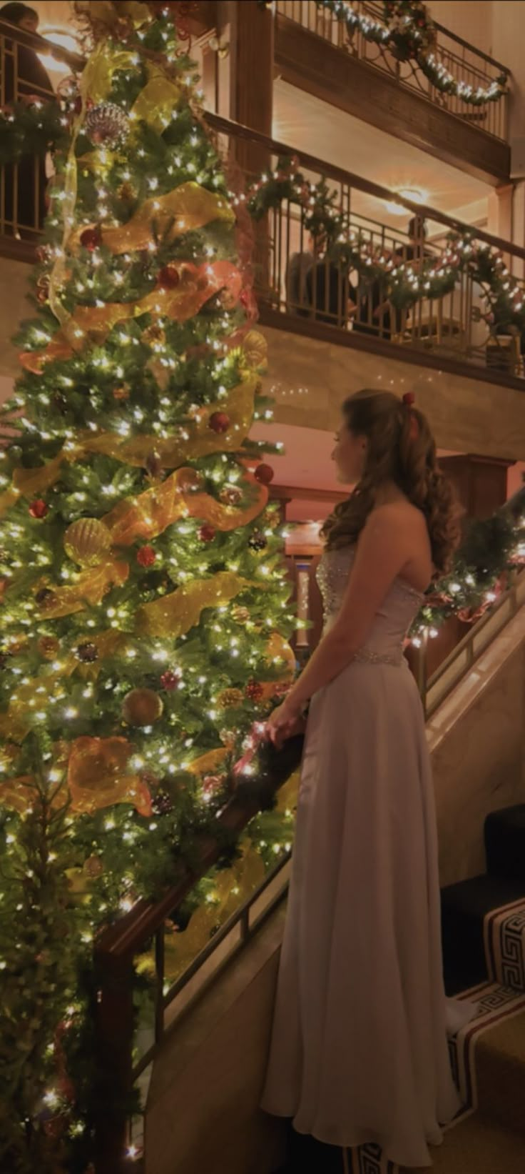 a woman in a white dress standing next to a christmas tree with lights on it