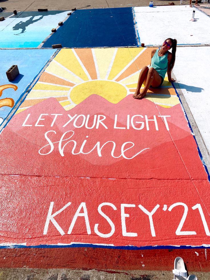 a woman sitting on the ground next to a sign that says let your light shine kasey'21