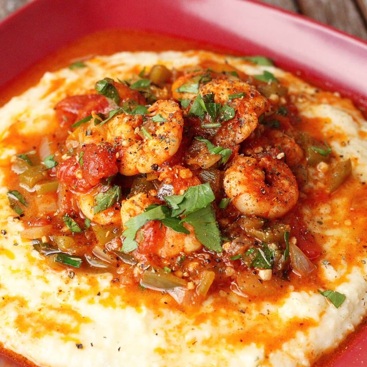 a red plate topped with mashed potatoes covered in shrimp and garnished with cilantro