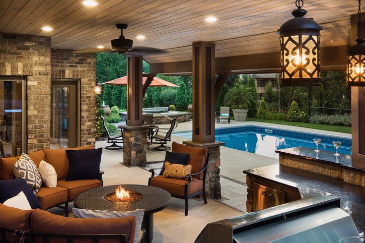 an outdoor living area with fireplace, couches and tables next to a swimming pool