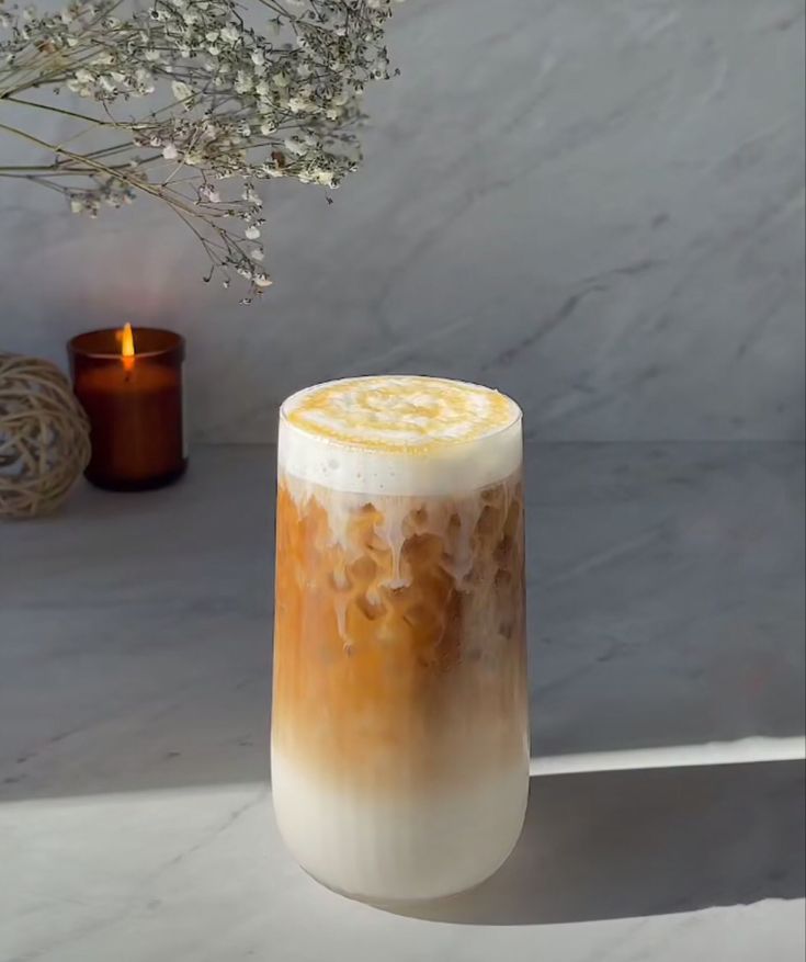 there is a tall glass with liquid in it next to a candle and some flowers