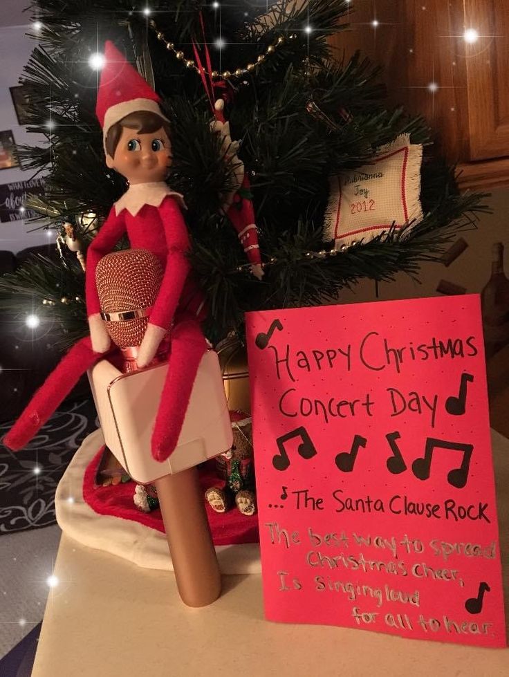 an elf is sitting on top of a christmas tree next to a sign that says happy christmas concert day