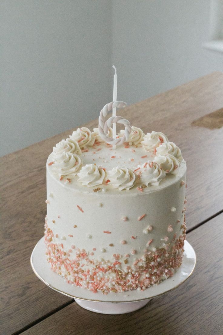 a white cake with sprinkles and a single candle on it sitting on a table