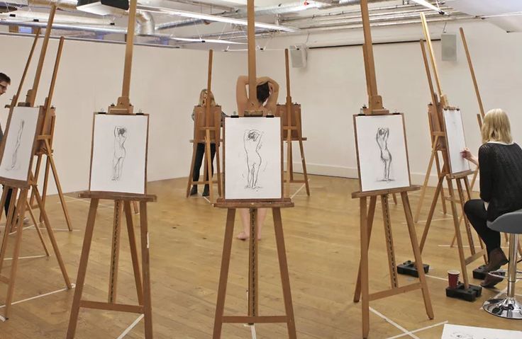 people are standing around in an art studio with easels and paintings on the floor