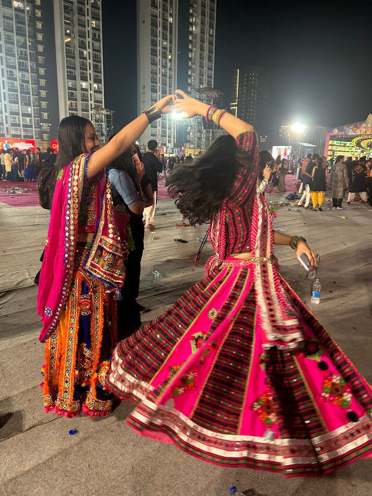 two women in colorful dresses dancing on the street at night with buildings in the background