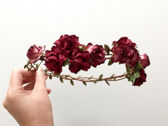 a hand holding a flower crown with red flowers on it's head and green leaves