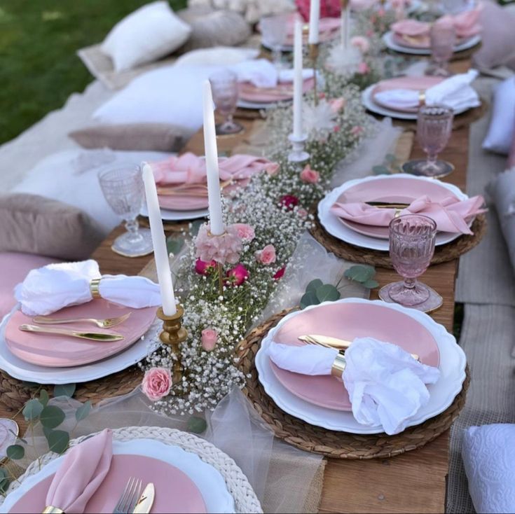 the table is set with pink and white plates, napkins, candles and flowers