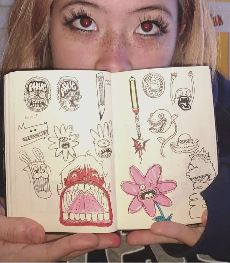 a woman is holding an open book with drawings on it and looking at the camera