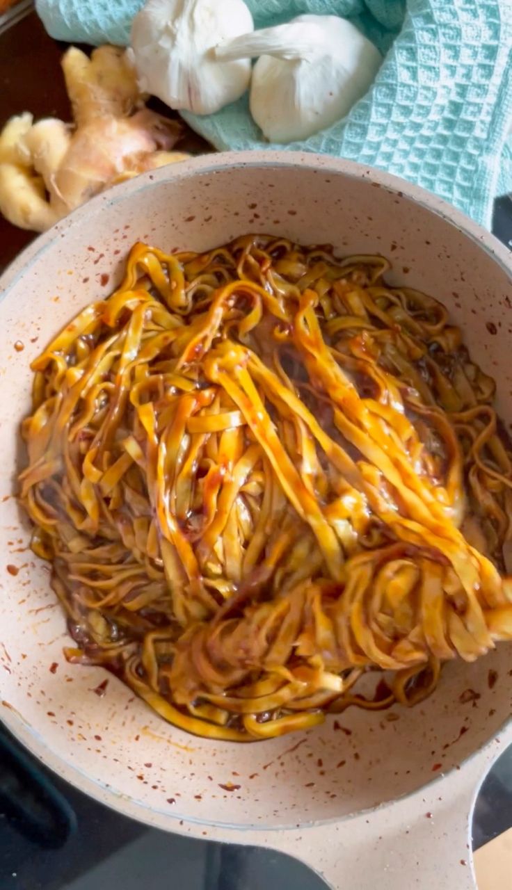 a bowl filled with noodles and sauce on top of a table next to garlic cloves