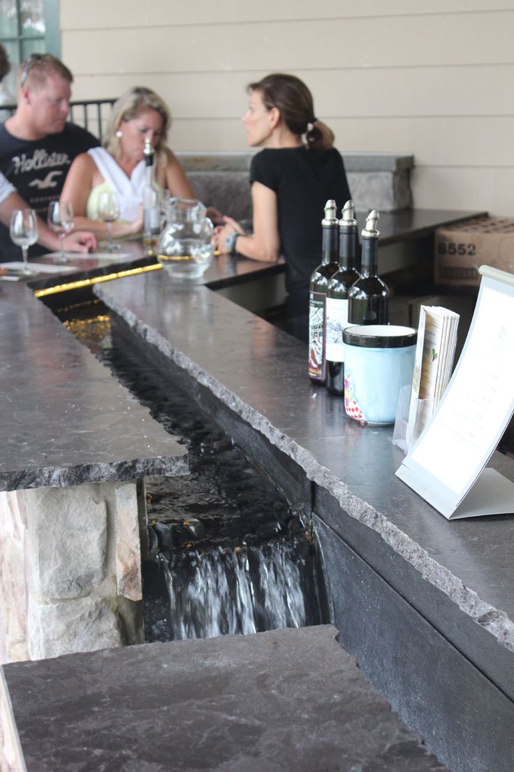 several people sitting at a bar with bottles and wine glasses on the counter next to them