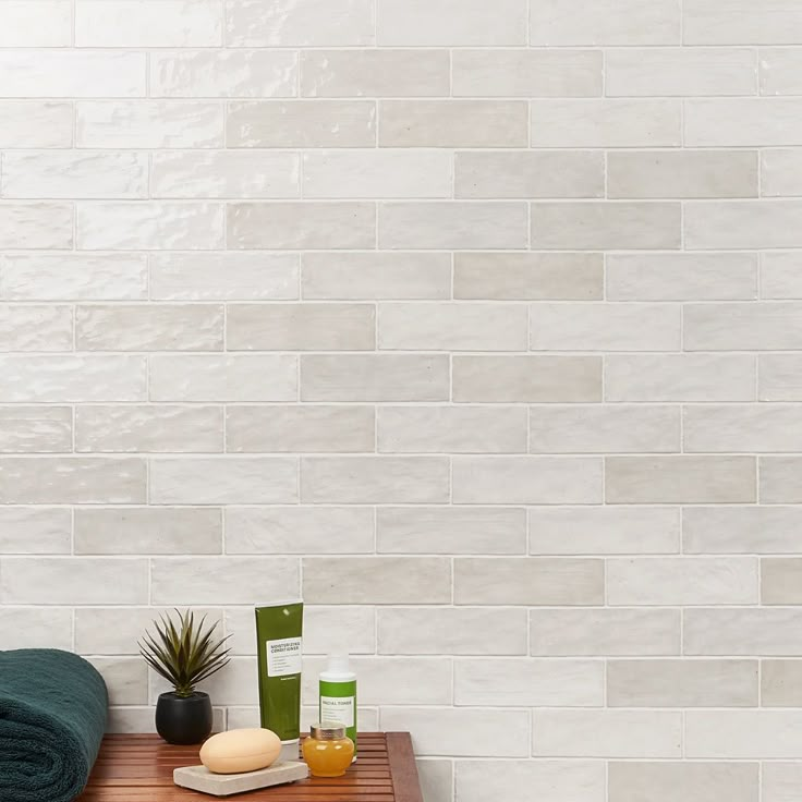 a wooden table topped with green towels and other bathroom items next to a white tiled wall