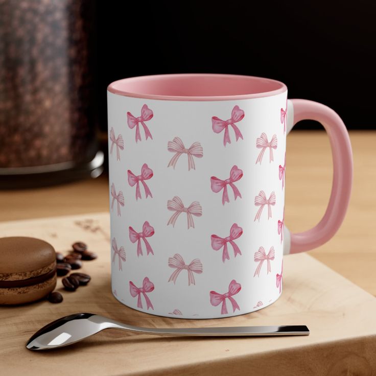 a pink and white coffee mug with bows on it next to a cup of coffee