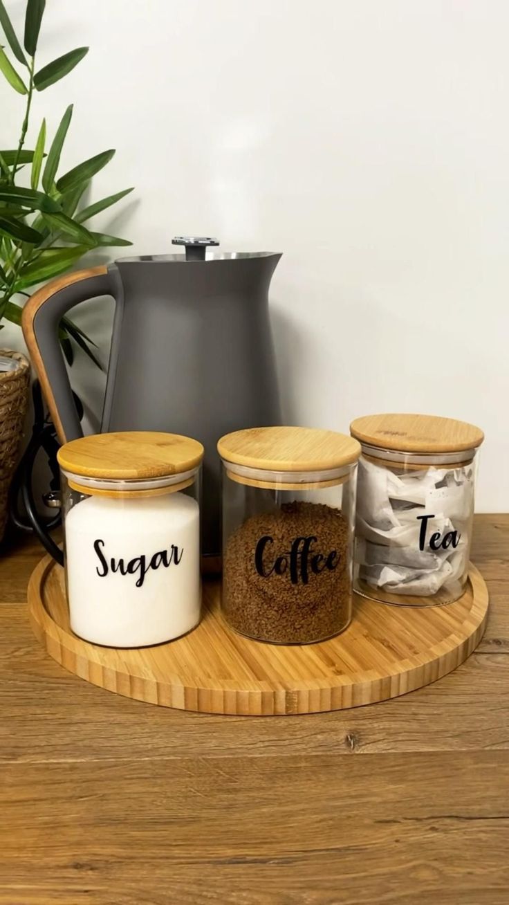 three jars with coffee and sugar on a wooden tray next to a potted plant