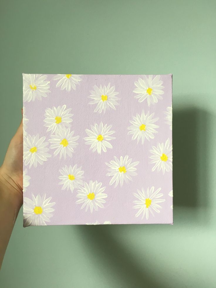 a hand holding up a piece of paper with white daisies on it and yellow centers