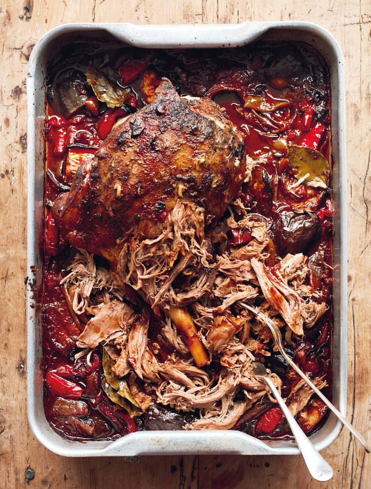 a roasting pan filled with meat and vegetables on a wooden table next to utensils