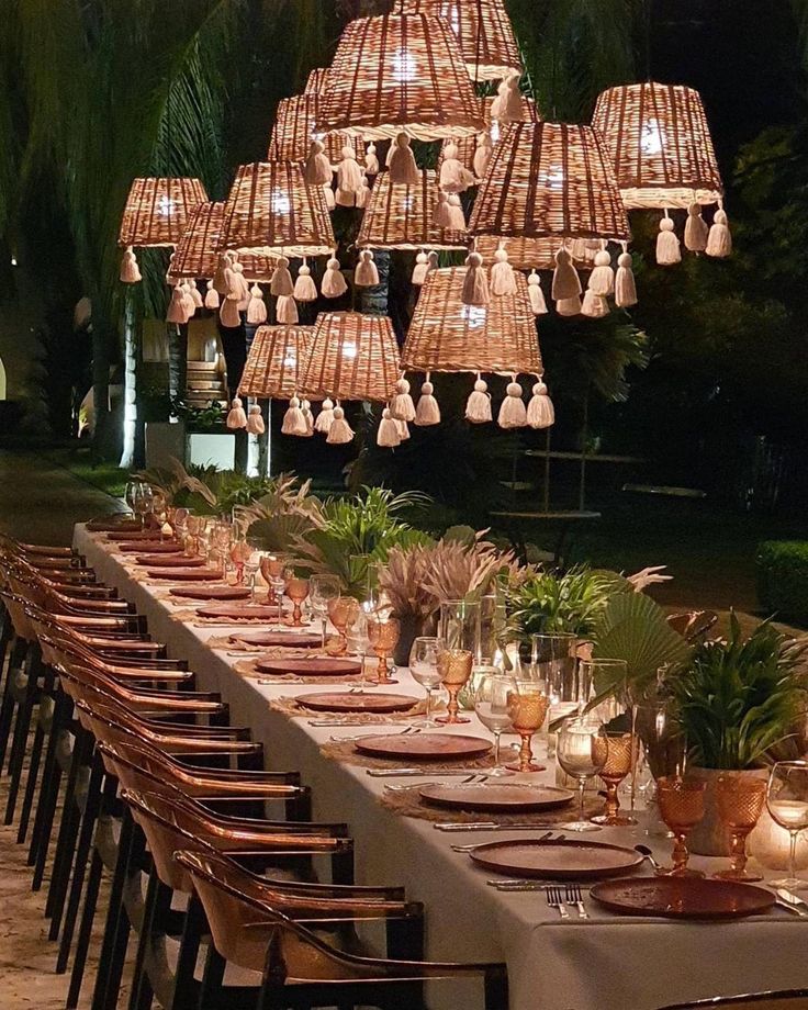 a long table with many plates and place settings on it, surrounded by hanging lights