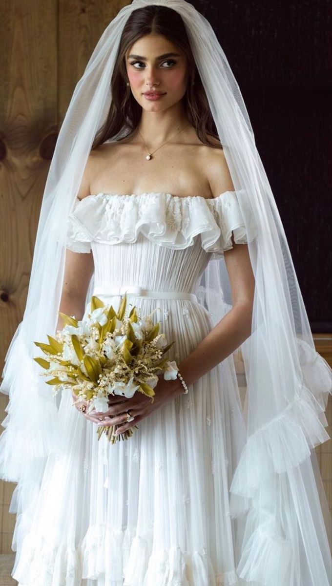 a woman in a white wedding dress holding a bridal bouquet and wearing a veil