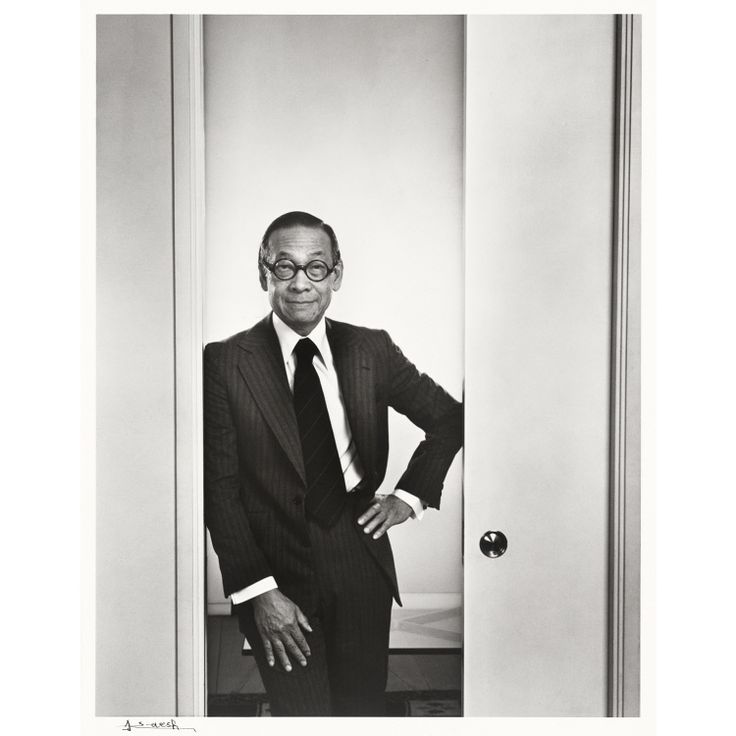 a black and white photo of a man in a suit standing next to an open door