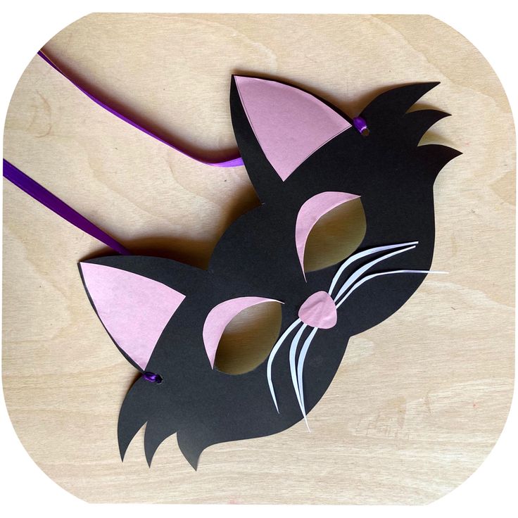 a black cat mask with pink ears on a wooden table next to a purple ribbon