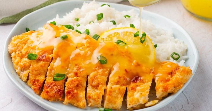 a white plate topped with chicken covered in cheese and sauce next to rice, lemon wedges and a glass of orange juice