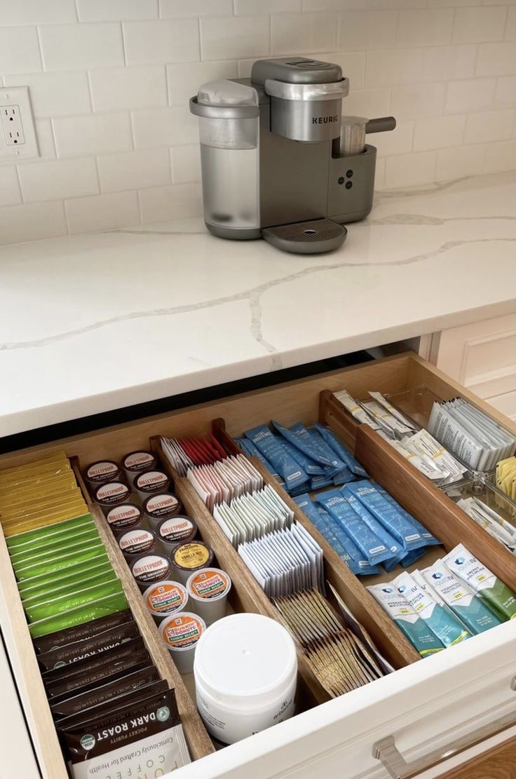 an open drawer in a kitchen filled with chocolates and other food items next to a coffee maker