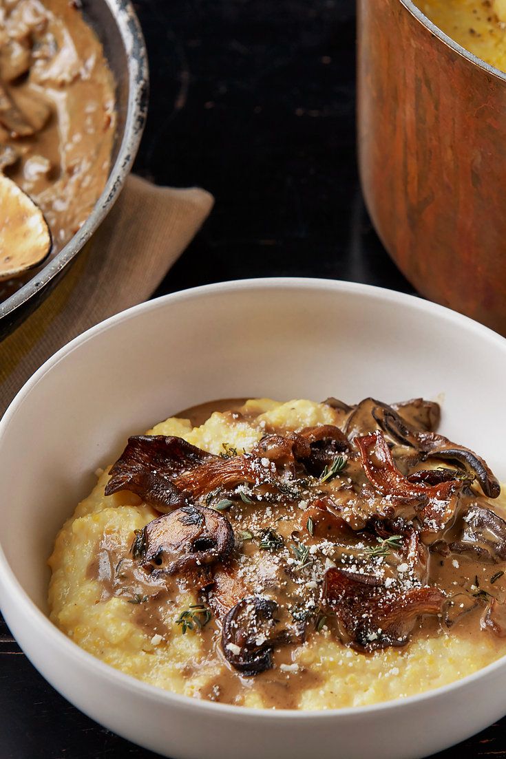 a white bowl filled with mashed potatoes and mushrooms next to a pot of mushroom gravy