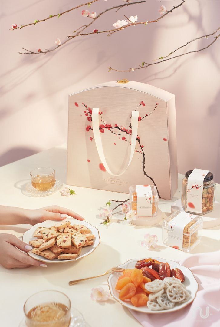 two people holding plates of food on a table next to a paper bag with flowers in it