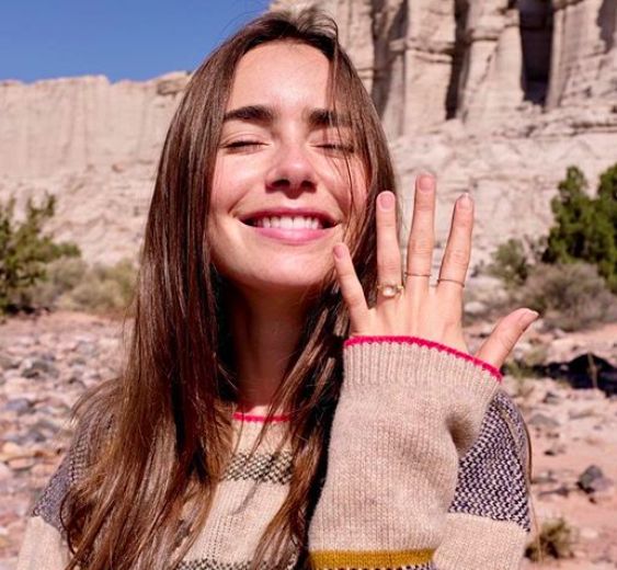 a woman with long hair is smiling and holding her hand up to her face in the desert