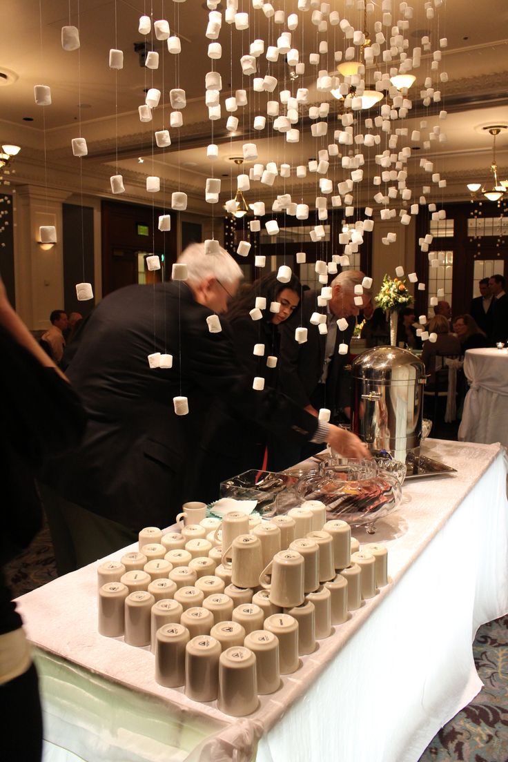 several people standing around a table with cups on it and hanging from the ceiling in front of them