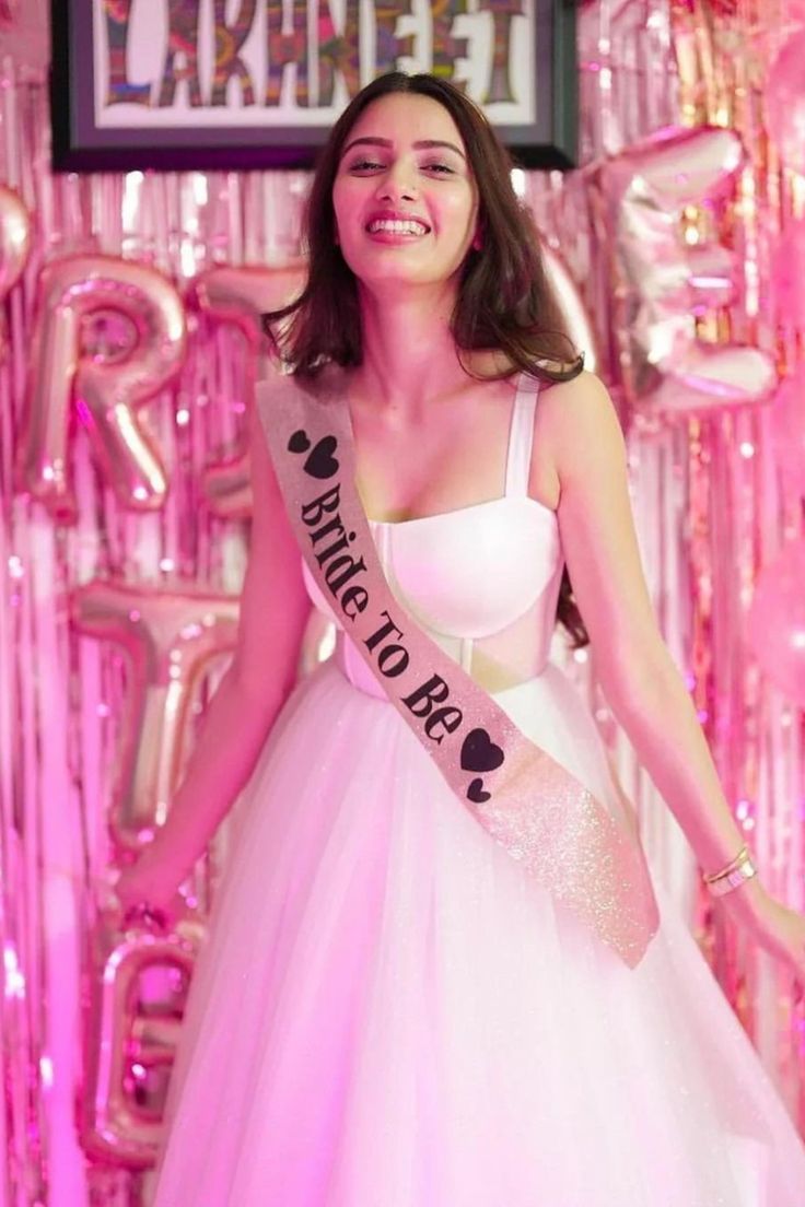 a woman in a pink and white dress is standing on stage with balloons behind her