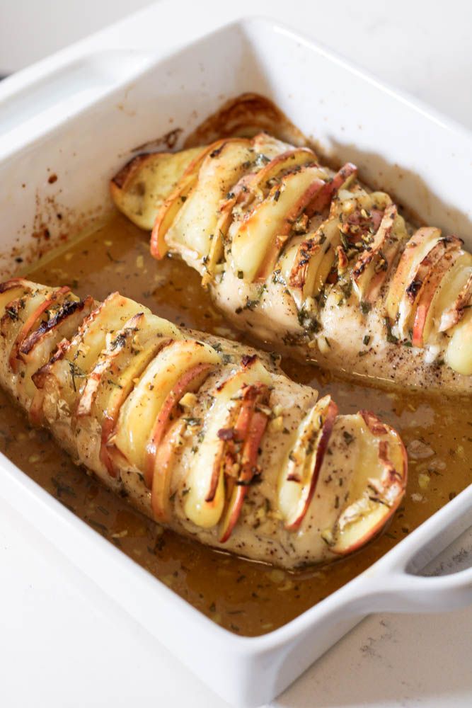 two pieces of chicken covered in apples and spices sitting in a casserole dish