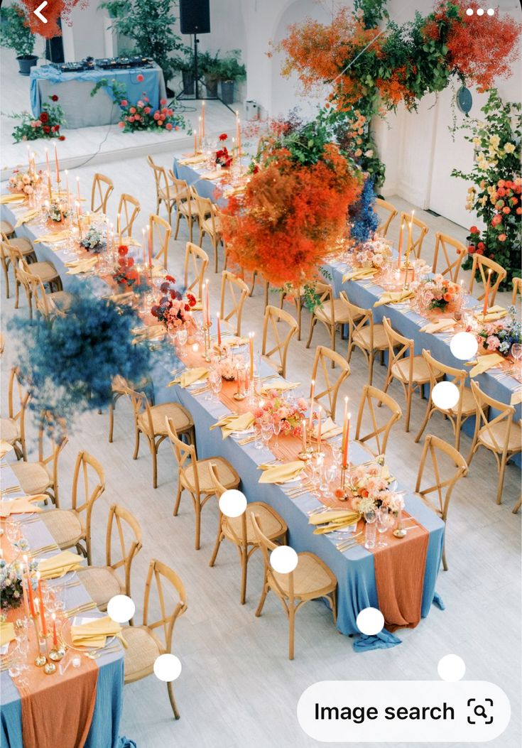 a long table set up with blue linens and orange flowers in the center for an event