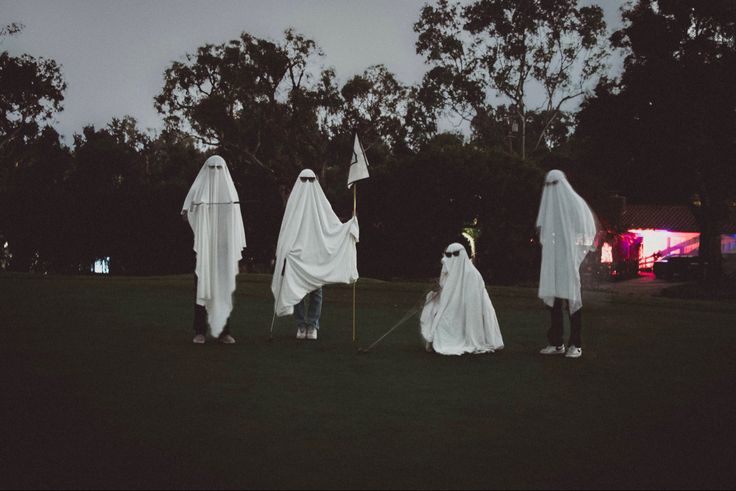 three people in ghost costumes holding flags and standing on the grass with trees in the background