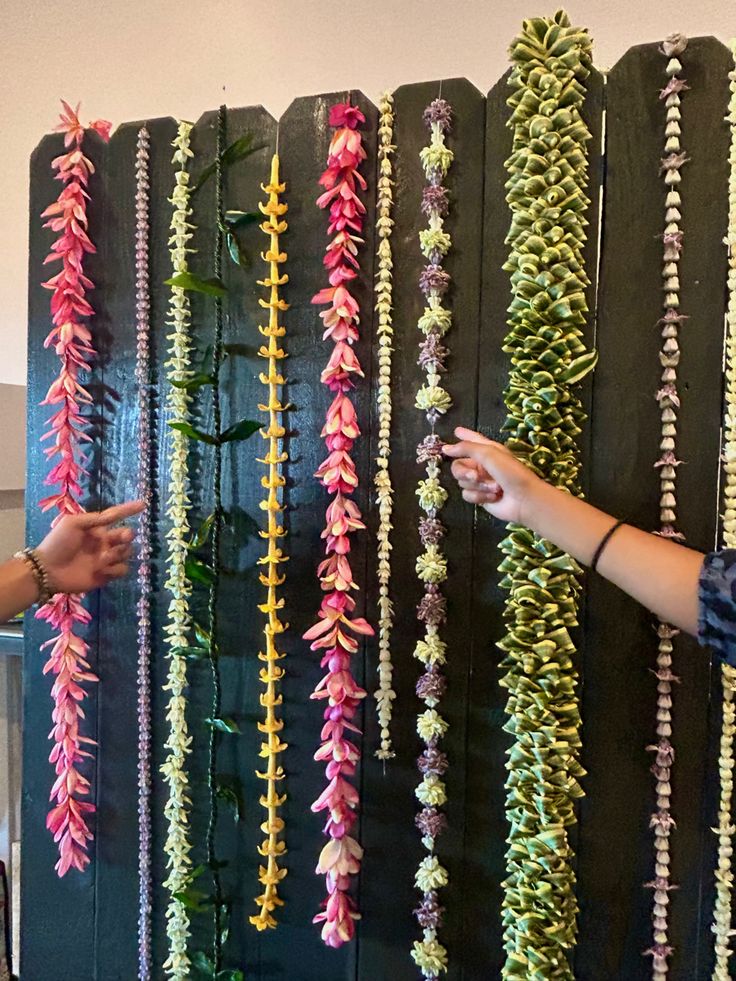 two people pointing at some colorful flowers on a black board with green and pink strips