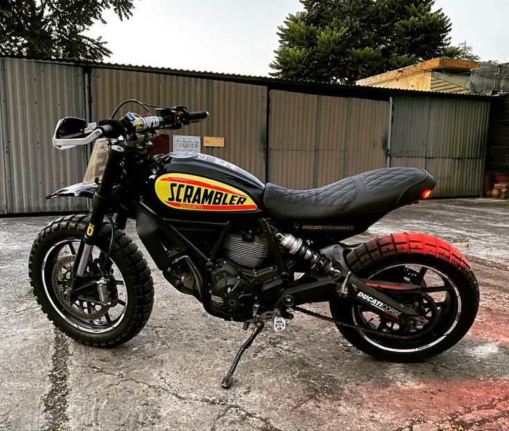 a black and yellow motorcycle parked in front of a metal building with graffiti on it